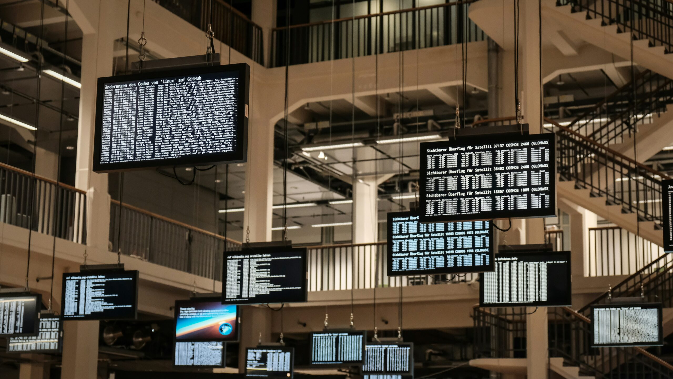 A bunch of televisions screens hanging from the ceiling and displaying data